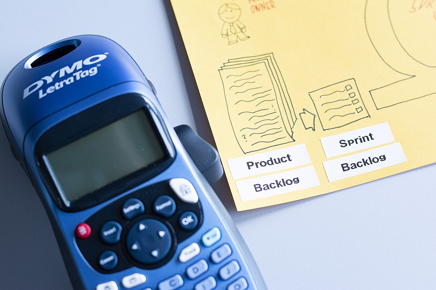 DYMO LetraTag Gerät neben einer Zeichnung mit den Begriffen „Product Backlog“ und „Sprint Backlog“, die per Etikett beschriftet wurden.