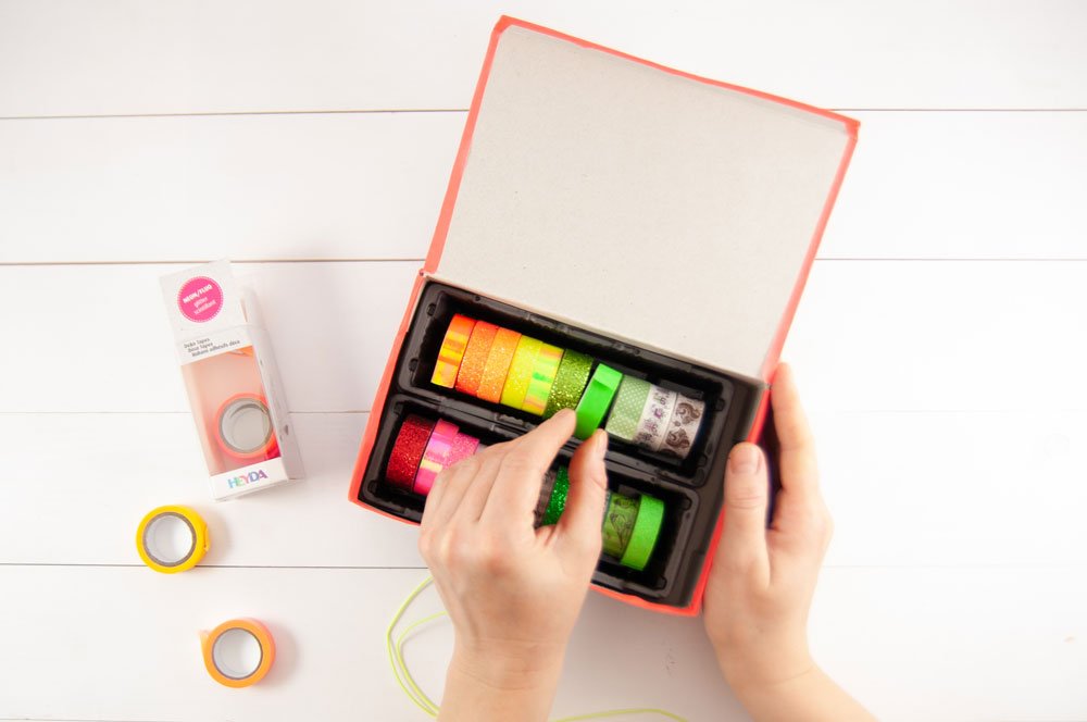 Hände legen buntes Washi-Tape in selbstgebastelte Ordnungsbox