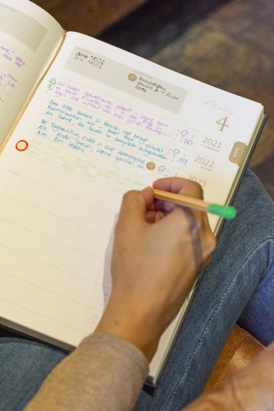 Nahaufnahme aus der Vogelperspektive auf einen aufgeschlagenen 10 Jahreskalender der Marke Brunnen, in dem für die Jahre 2021-2023 schon etwas eingetragen ist und mit einem grünen Fineliner noch etwas hinzugefügt wird.