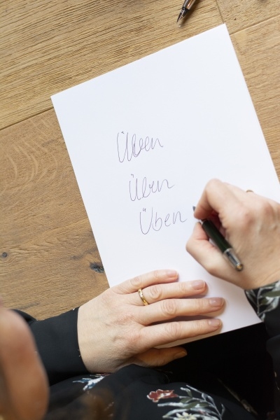 Frau schreibt "Üben, üben, üben" auf ein Blatt Papier.