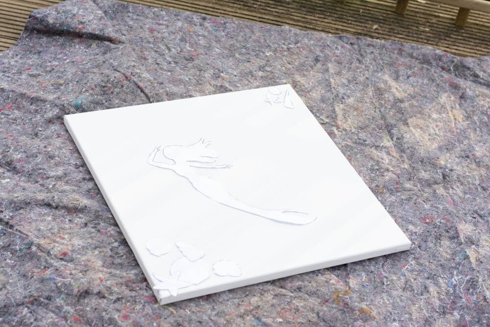 Eine Leinwand mit Schablonen, die eine Meerjungfrau und Muscheln darstellen, liegt auf einer Malerdecke.