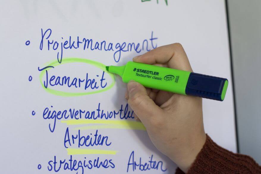 Eine Hand umkreist mit dem Textmarker Textsurfer von Staedtler in grün das Wort "Teamarbeit" auf einem Flipchart.