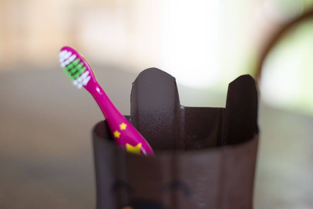 In einem braunen Zahnputzbecher steht eine rosa-gelbe Kinder-Zahnbürste.