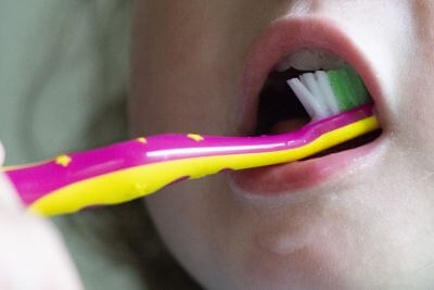 Ein Kind putz seine Zähne mit einer pink-gelben Zahnbürste.