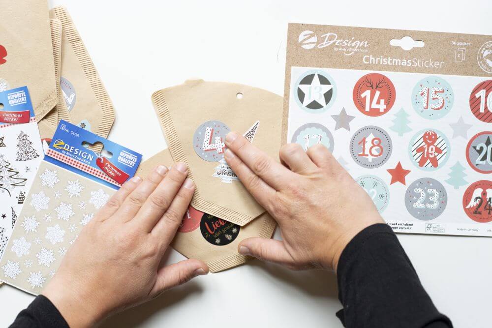 Kaffeefilter werden mit Christmasstickern mit Zahlen darauf von Avery Zweckform beklebt. 