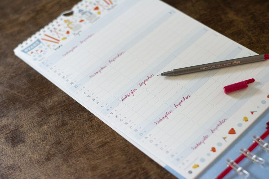 Nahaufnahme eines nahezu leeren Blatts in einem Familienplaner von Heye: Nur das Wort "Wochenplan besprechen" ist mit Rotstift eingetragen.