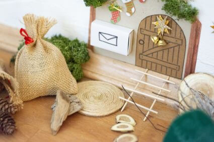 Nahaufnahme einer Wichteltür, die mit Bastelmaterialien von Heyda und Knorr Prandell gestaltet wurde: Eine kleine Dekobox dient als Briefkasten, ein kleiner Jutesack steht daneben.