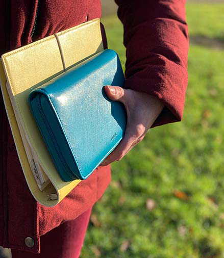Eine Person mit einer roten Jacke steht im Grünen. Die Sonne scheint auf zwei Planer der Marke Filofax, die die Person in der Hand hält. 