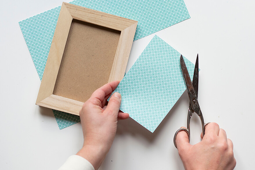 Anleitung für einen Do-it-yourself-Scherenschnitt. Schritt 4: Ein Blatt mintfarben und grafisch gemusterter Motiv-Fotokarton wird als Hintergrundpapier auf die Größe des Bilderrahmens zugeschnitten. 