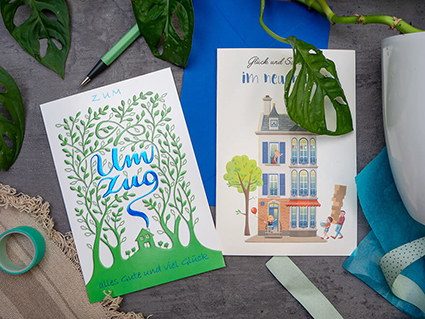 Auf einem anthrazitfarbenen Untergrund liegen zwei Grußkarten des ABC Glückwunschkartenverlags. Auf der linken Karte ist ein kleines Haus zwischen hohen knorrigen Bäumen zu sehen. Aus dem Schornstein des Hauses steigt Rauch auf. Er bildet das Wort "Einzug". Auf der rechten Karte ist ein hohes, buntes Stadthaus zu sehen. Zwei Personen schleppen Umzugskarton hinein. Auf der Karte steht: "Glück und Sonnenschein im neuen Heim". Foto: Johanna Rundel