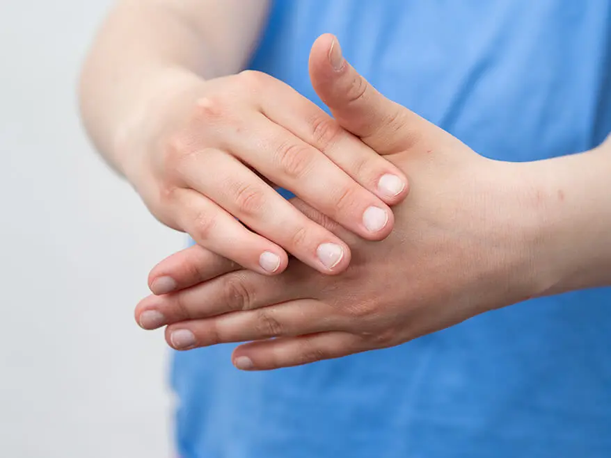 Eine Person in einem blauen T-Shirt massiert sich mit der rechten Hand die linke Hand.