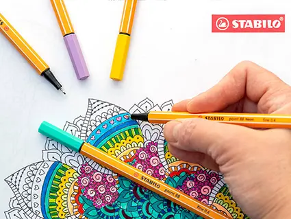 Jemand malt mit Finelinern von Stabilo Details in einem ausgedruckten Mandala kleine Herzen aus.