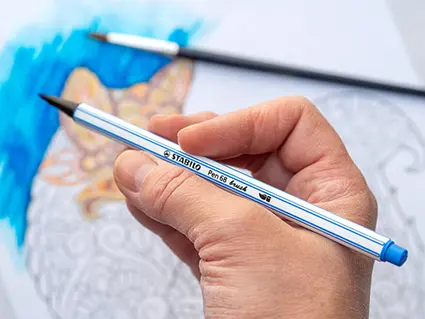 Jemand hält einen wasservermalbaren Filzstift von Stabilo vor ein halb ausgemaltes Fuchs-Mandala mit Aquarelleffekt.