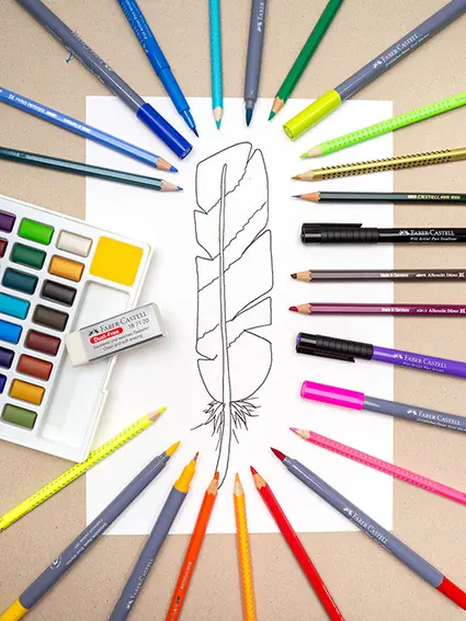 Um eine gemalte Vogelfeder auf einem weißen Blatt liegen verschiedene Künstlerfarben und Stifte von Faber-Castell in einem Oval. Foto: Johanna Rundel