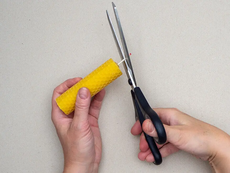 Jemand kürzt den Docht einer aus Bienenwachsplatten von KNORR prandell gerollten Kerze mit einer Schere. Foto: Johanna Rundel