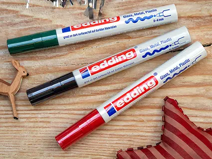 Ein roter, ein grüner und ein schwarzer Marker von edding liegen auf einer Holzoberfläche. Foto: Johanna Rundel