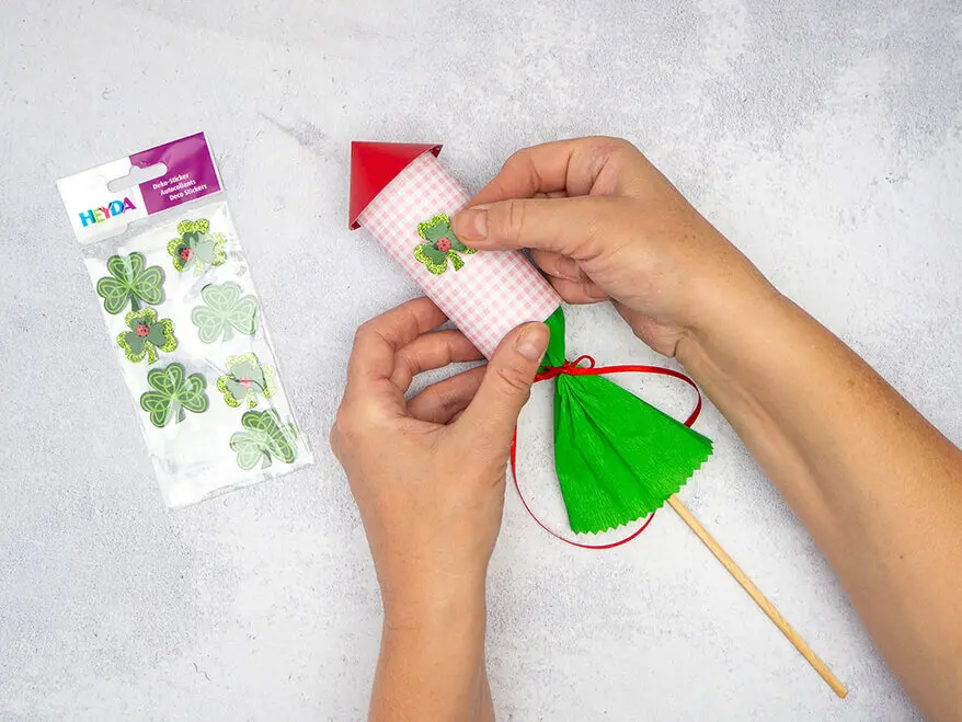 Jemand klebt einen Kleeblatt-Aufkleber von HEYDA auf die Außenseite einer selbstgebastelten Silvesterrakete aus Papier. Foto: Johanna Rundel 