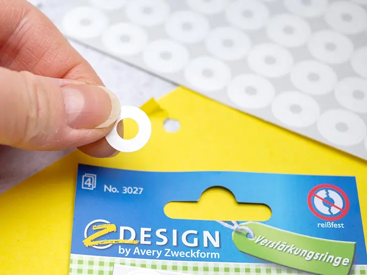 Jemand klebt einen Verstärkungsring von Avery Zweckform auf ein ausgerissenes Heftloch eines Dokuments. Foto: Johanna Rundel)