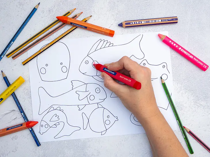 Jemand malt mit Bunt- und Wachsmalstiften von STAEDTLER eine Vorlage mit verschiedenen Fischen aus. Foto: Johanna Rundel