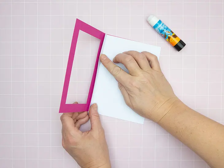 Jemand klebt mit einem Klebestift von Pelikan, eine weiße Trennseite in eine pinke Passepartoutkarte. Foto: Johanna Rundel