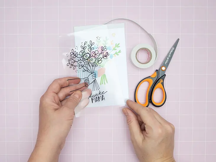 Jemand legt zwei mit Markern von Pelikan gestaltete, rechteckige Folien und ein ebenso großes weißes Blatt übereinander. Foto: Johanna Rundel