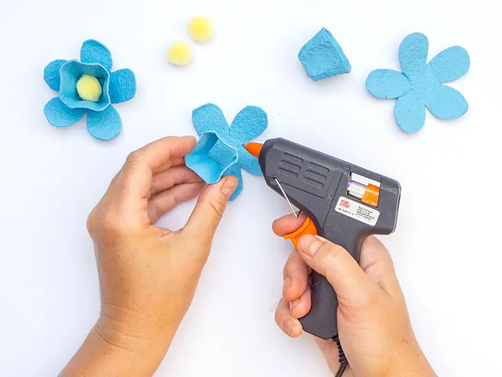 Jemand klebt mit einer Heißklebepistole von KNORR prandell eine blaue Blüte aus Eierkartonteilen zusammen. Foto: Johanna Rundel