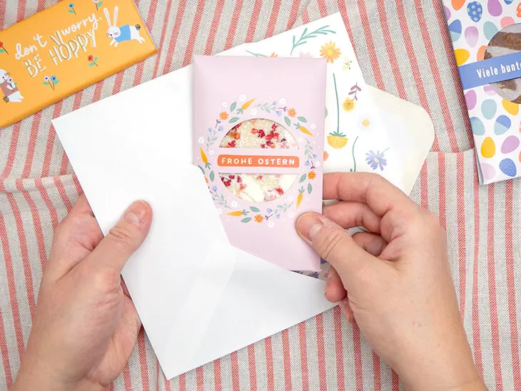 Jemand schreibt mit einem gelben Stift in eine Grußkarte von Grafik Werkstatt einen Spruch zu Ostern. Drumherum sind weitere Osterkarten verteilt. Foto: Johanna Rundel