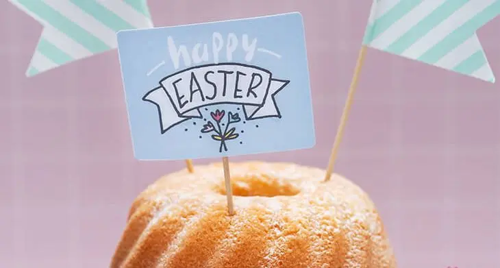 Ein heller Rührkuchen auf einer weißen Kuchen-Etagere. Im Kuchen stecken gestreifte Fähnchen und ein Caketopper mit Ostermotiv, der aus Etiketten von Avery Zweckform gestaltet wurde. Foto: Johanna Rundel