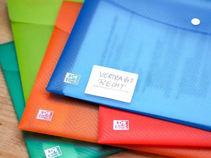 Verschiedenfarbige Sammelmappen von Oxford liegen übereinander. Auf der obersten klebt ein Aufkleber auf dem „Vertragsrecht“ steht. Foto: Johanna Rundel