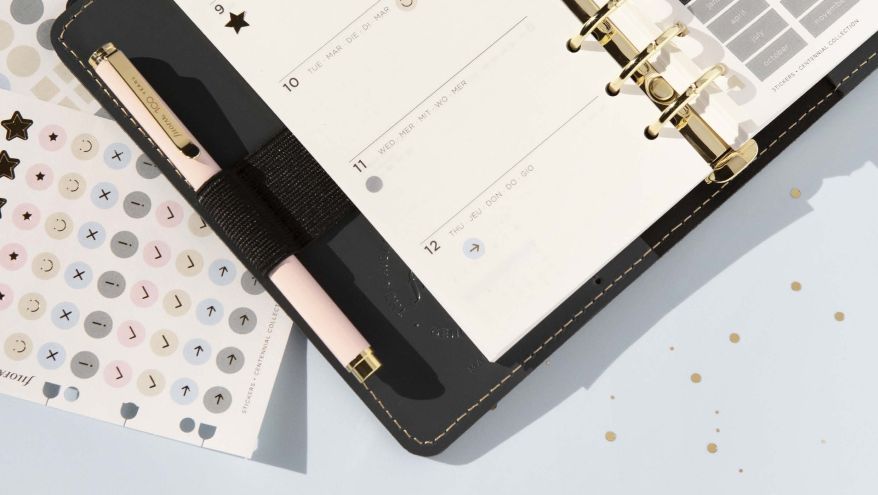 Aufgeschlagener Filofax-Planer mit Stift in der Stiftschlaufe. Daneben Sticker mit Icons.