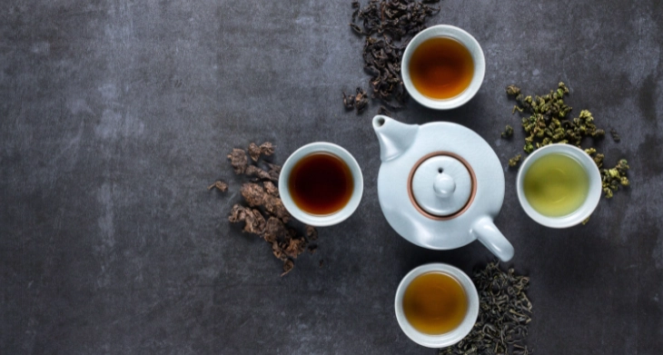 Verschiedene Teesorten in Tassen mit losen Blättern, Früchten und Blüten