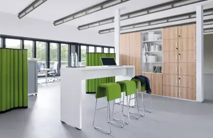 Büro mit weißem Hochtisch und grünen Hockern und grünen Trennwänden.