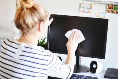Ein Bild, das eine junge Frau zeigt, die einen Computerbildschirm mit einem Reinigungstuch reinigt.