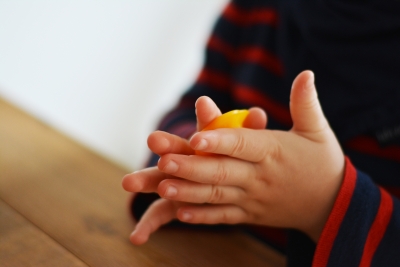 Kinderhände rollen gelben Knetbienenwachs zwischen den Händen.