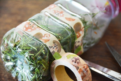 Eine mit Tannennadeln gefüllte Plastikflasche wird mit Masking-Tape verzeirt.