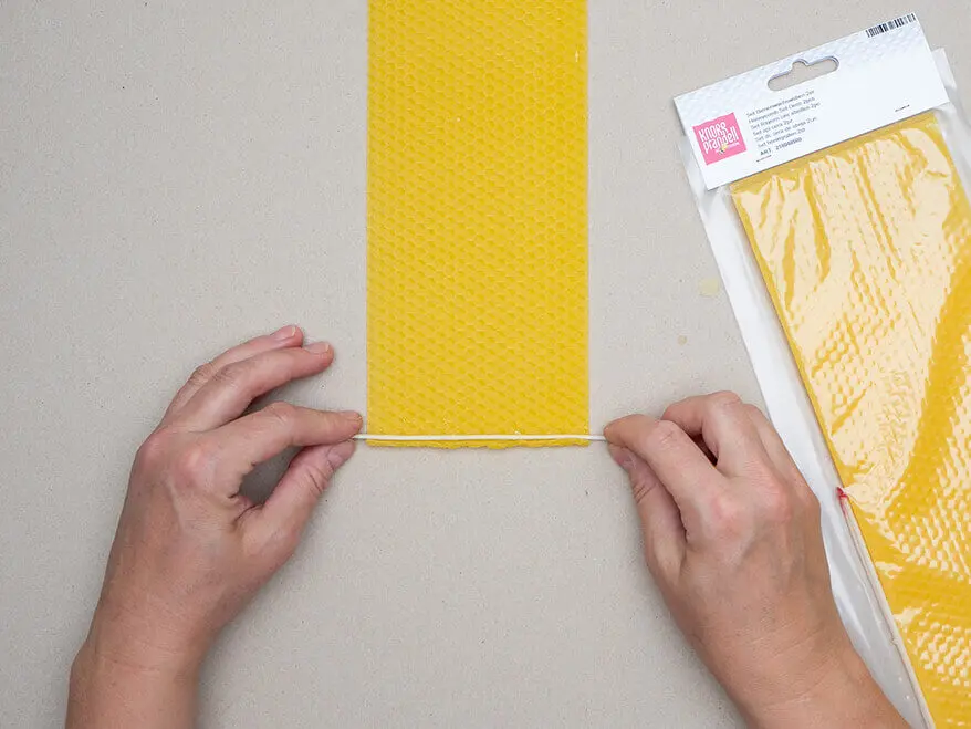 Jemand legt einen Docht auf die kurze Seite einer Bienenwachsplatte von KNORR prandell. Foto: Johanna Rundel