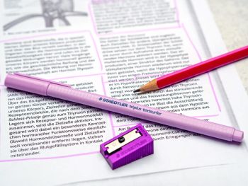Ein lila Textmarker und Spitzer sowie ein Bleistift von STAEDTLER liegen auf einem Schultext über Hormone. Foto: Johanna Rundel