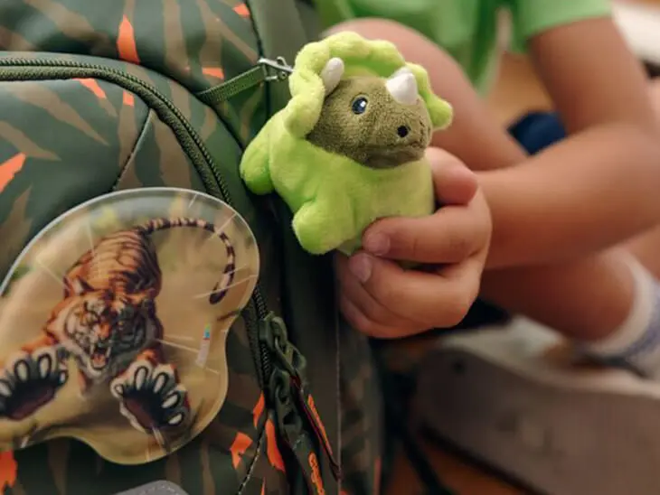 Ein Kind hält einen grünen Dino-Hangie von ergobag in die Kamera.