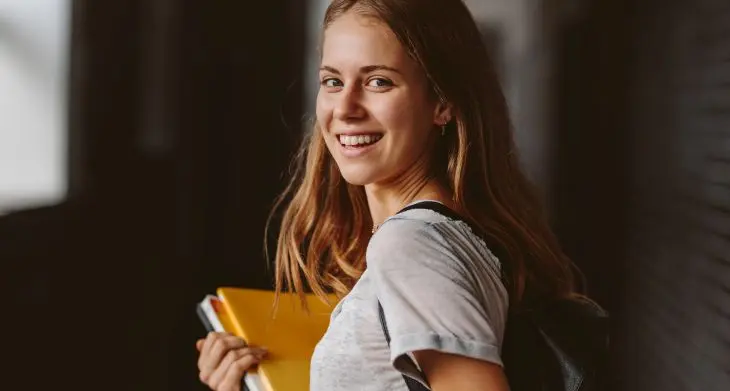 Eine junge Frau hält Collegeblöcke von Oxford im Arm und blickt lächelnd über die Schulter.