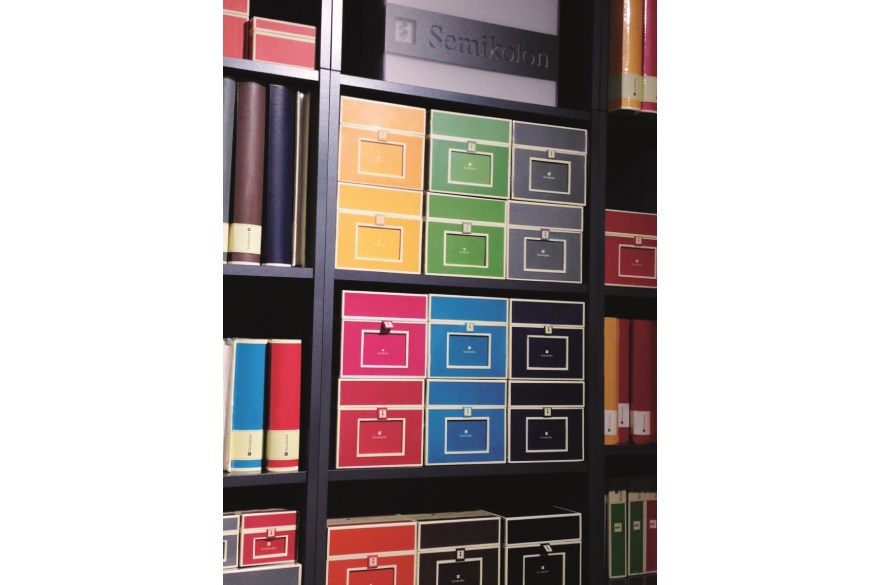 Semikolon Produkte farblich sortiert in einer Schrankwand.