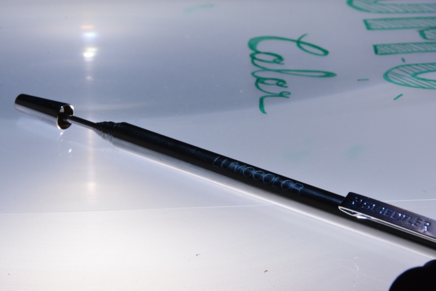 Auf einer Overhead Folie mit der Aufschrift "Lumocolor" liegt ein Zeigestab der Marke Staedtler.