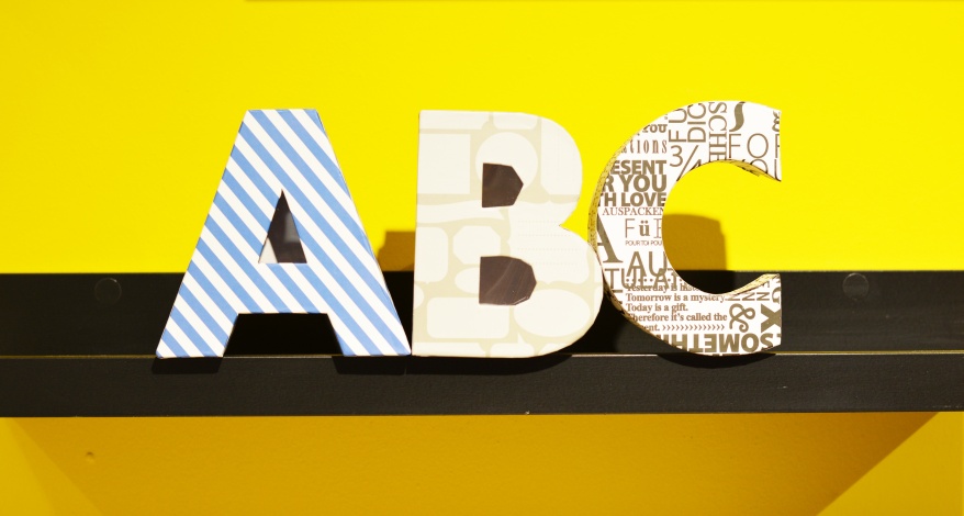 Vor einer gelben Wand stehen gemusterte Buchstaben A, B und C.