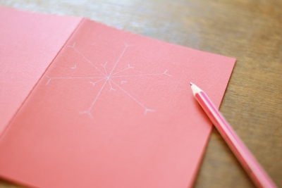 Schneeflocke mit Bleistift auf roter Karte vorgezeichnet