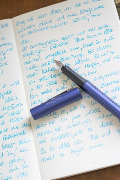 Auf einem aufgeklappten Tagebuch liegt ein lila Grip-Füller der Marke Faber-Castell.