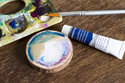 Baumscheibe wird mit Acrylfarben bunt bemalt, Farbpalette im Hintergrund