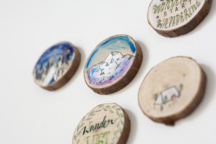 Fünf bemalte Baumscheiben mit Sprüchen und Wander-Motiven an der Wand