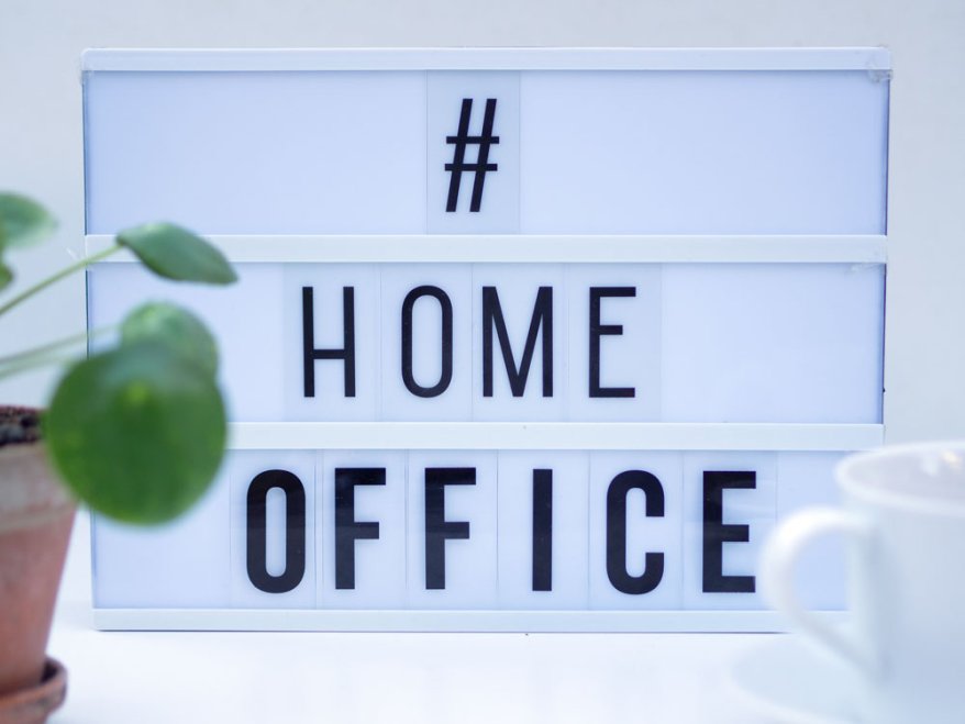 Leuchttafel mit Schriftzug „#HOME OFFICE“ auf weißem Tisch.