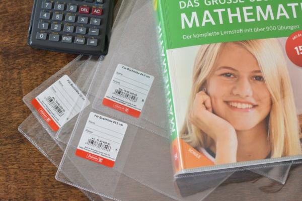 Ein Buch ist mit einem Buchschoner eingeschlagen, weitere Buchschoner liegen daneben.