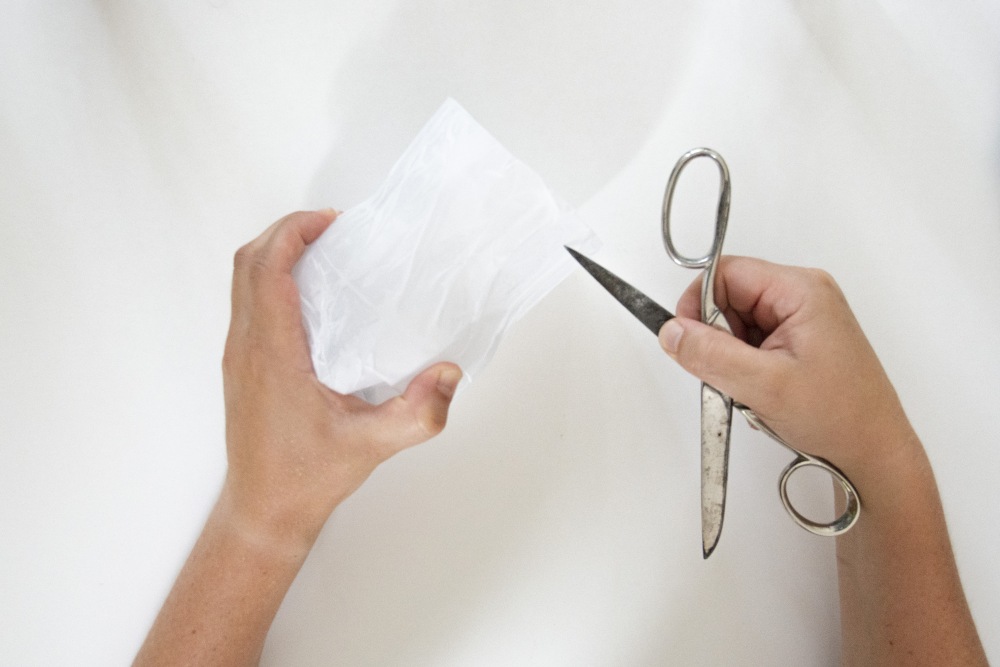 Hände schneiden mit einer Schere ein weißes, zerknittertes Papier zurecht.