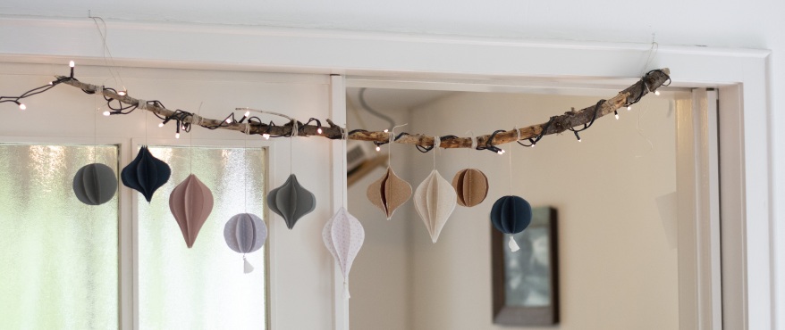 Weihnachtsgirlande aus Papier hängt an einem Ast mit Lichterkette im Wohnraum.